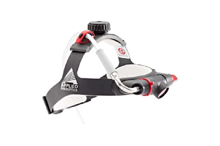 A black and white headgear device labeled "Applied Fiberoptics," equipped with cables, adjustment knobs, and magnifying lenses.